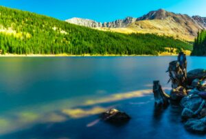 scenic view of the mountains with green pine trees beside calm body of water